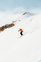 Person skiing down a mountain peak with a view of the summit in the background.